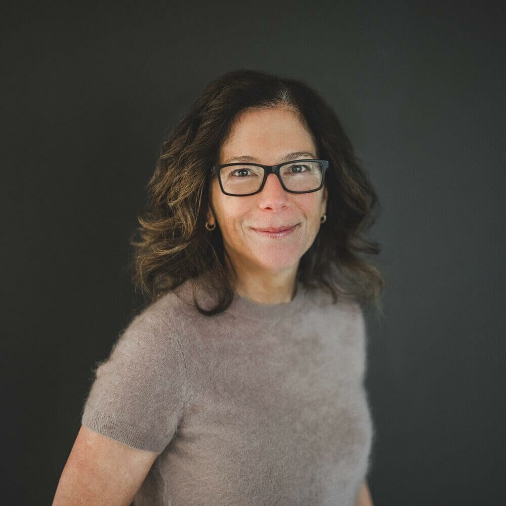 Smiling woman with glasses on dark background.