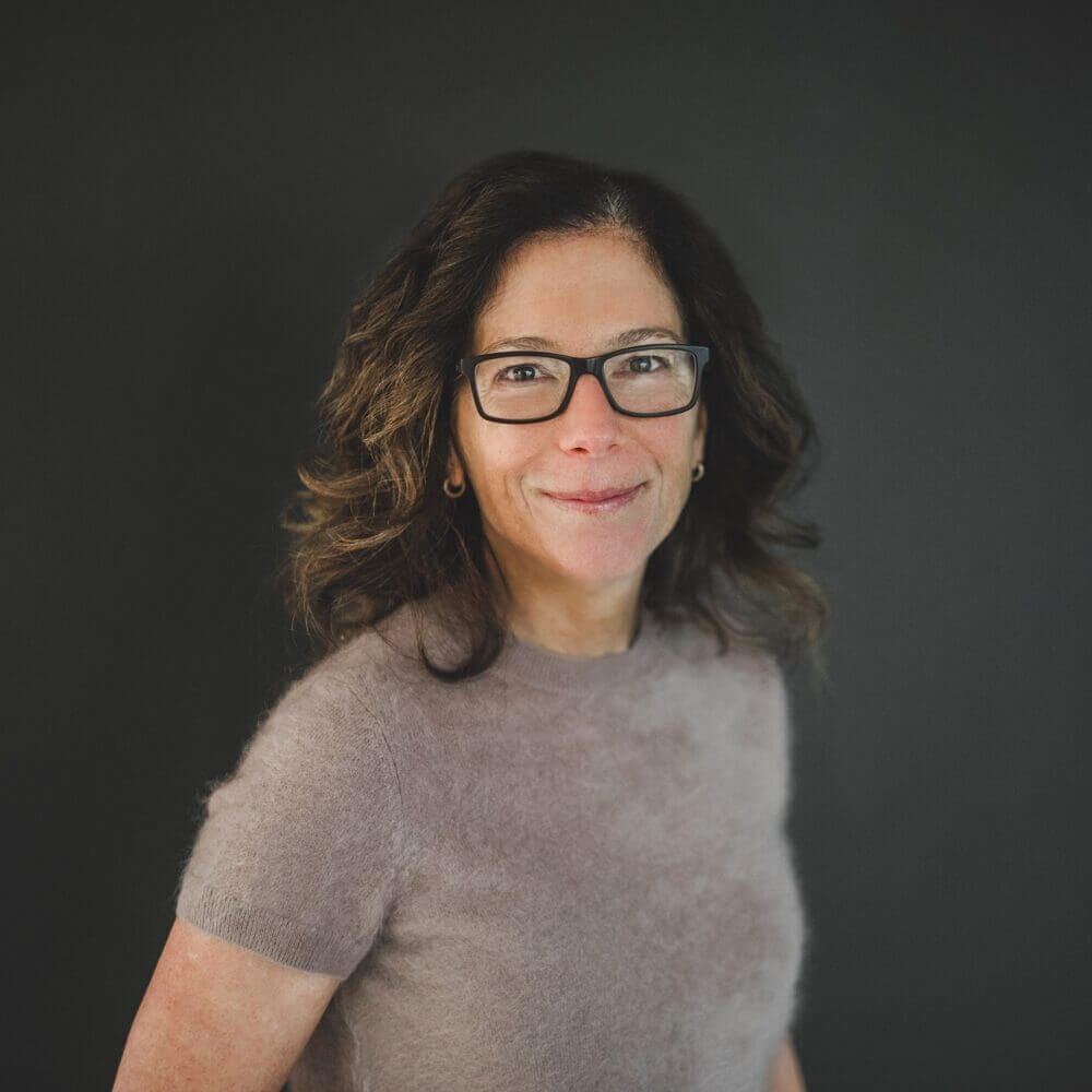 Smiling woman with glasses on dark background.